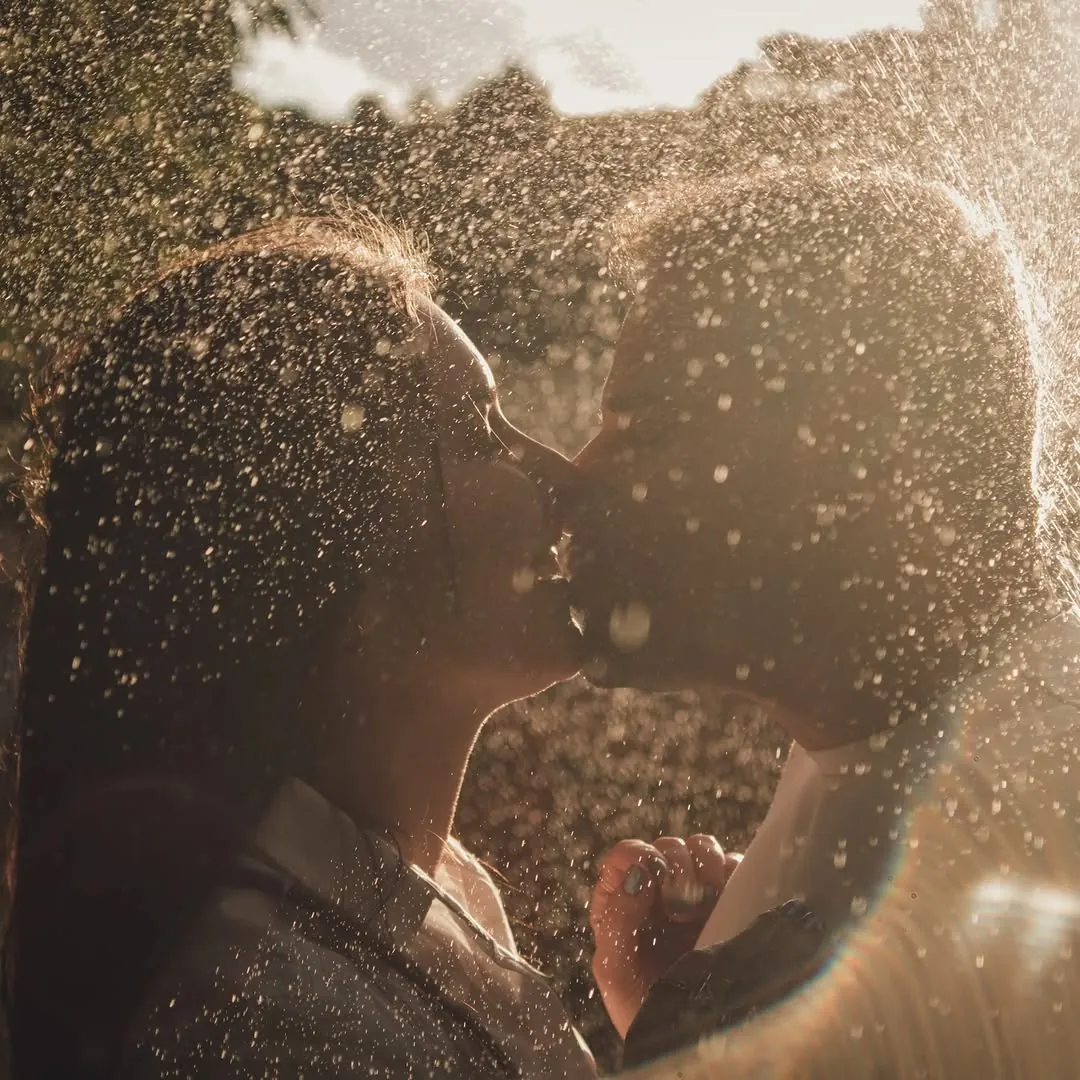 Casal se beija sob gotas de água iluminadas pelo sol do fim de tarde