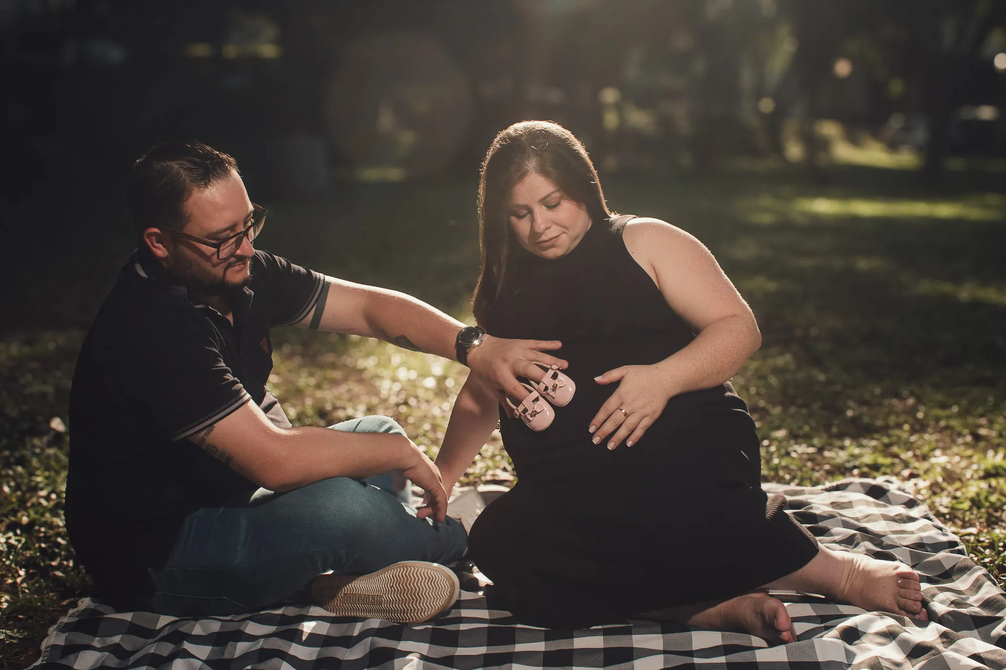 Casal sentado em piquenique, ele com a mão na barriga dela