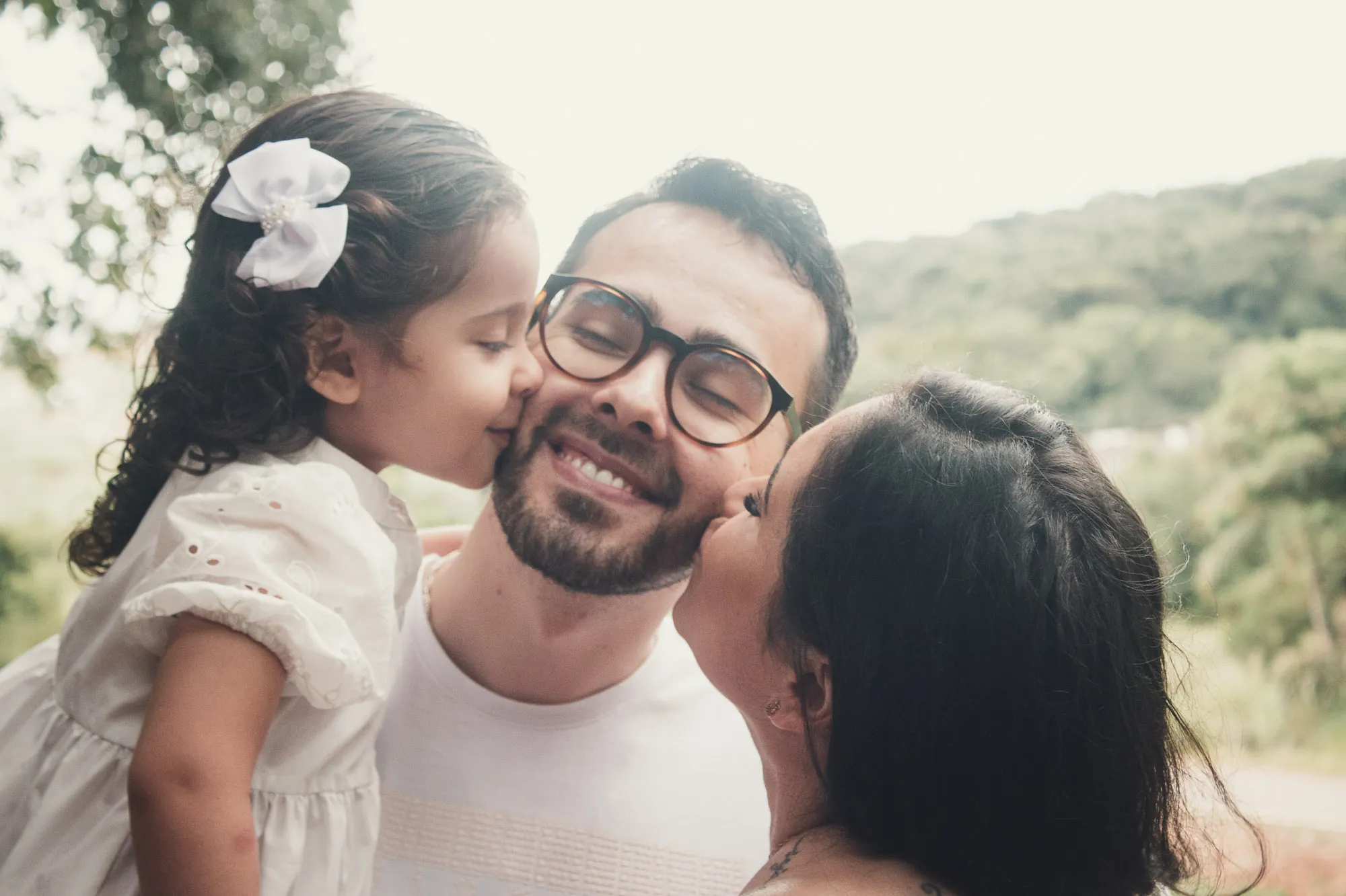 Filha e mãe beijam o pai nas bochechas