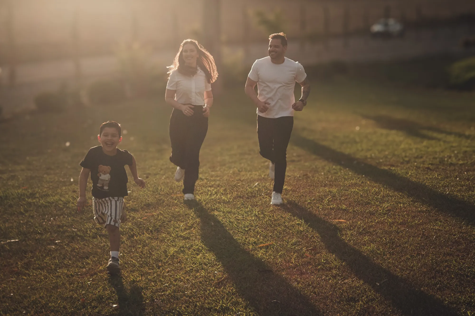 Pais e filho correm de mãos dadas num gramado ao fim da tarde