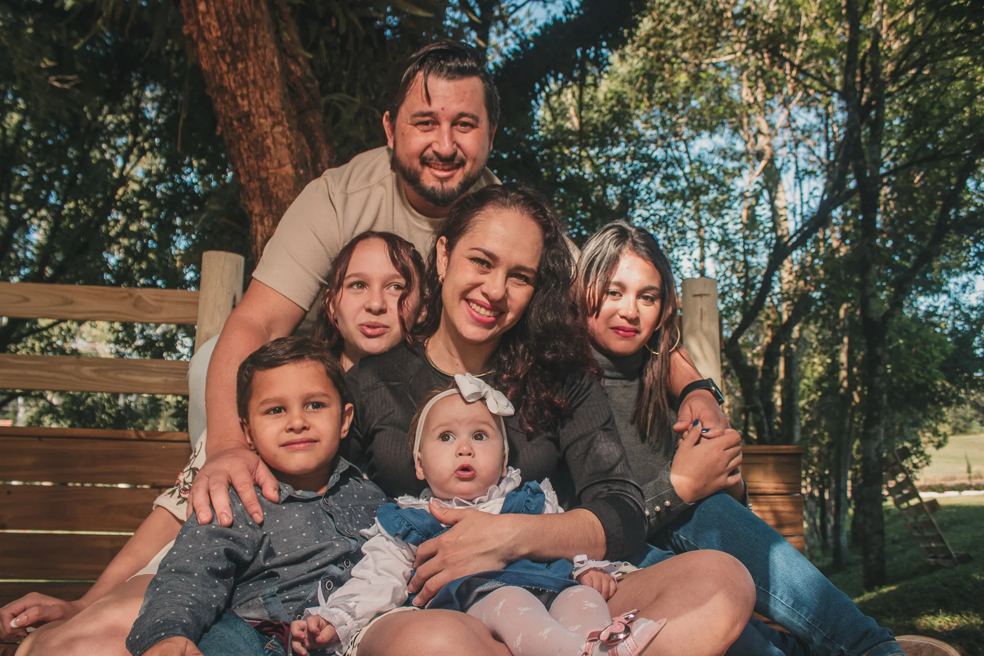 Família de seis abraçada em um banco de madeira