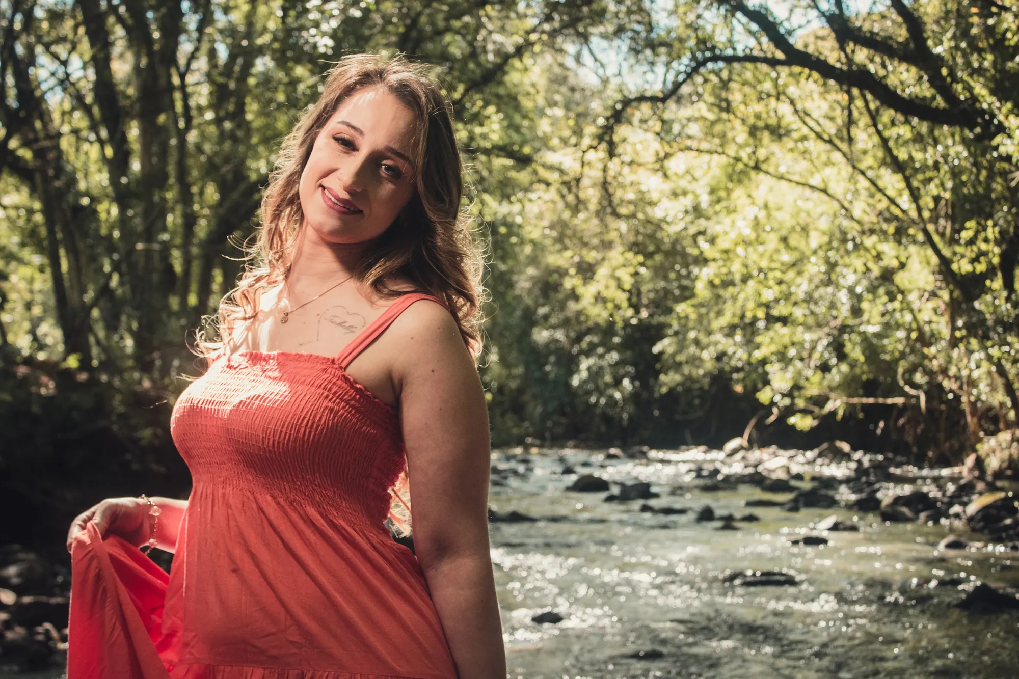 Gestante de vestido coral à beira de um rio