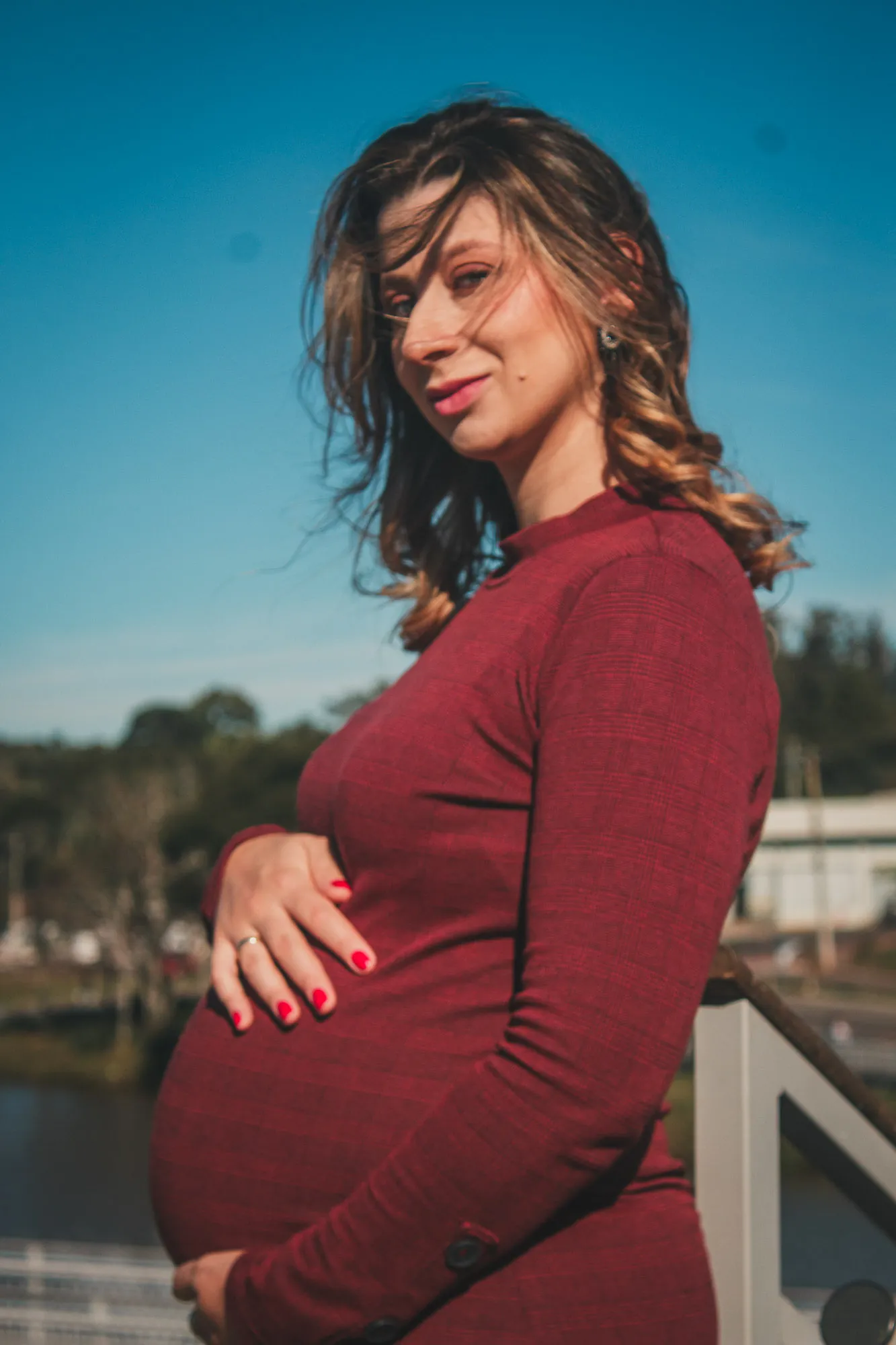 Gestante de vestido vermelho, mão na barriga, sob céu azul