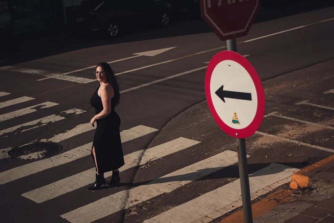 Mulher atravessa a faixa de pedestres ao lado de uma placa vermelha