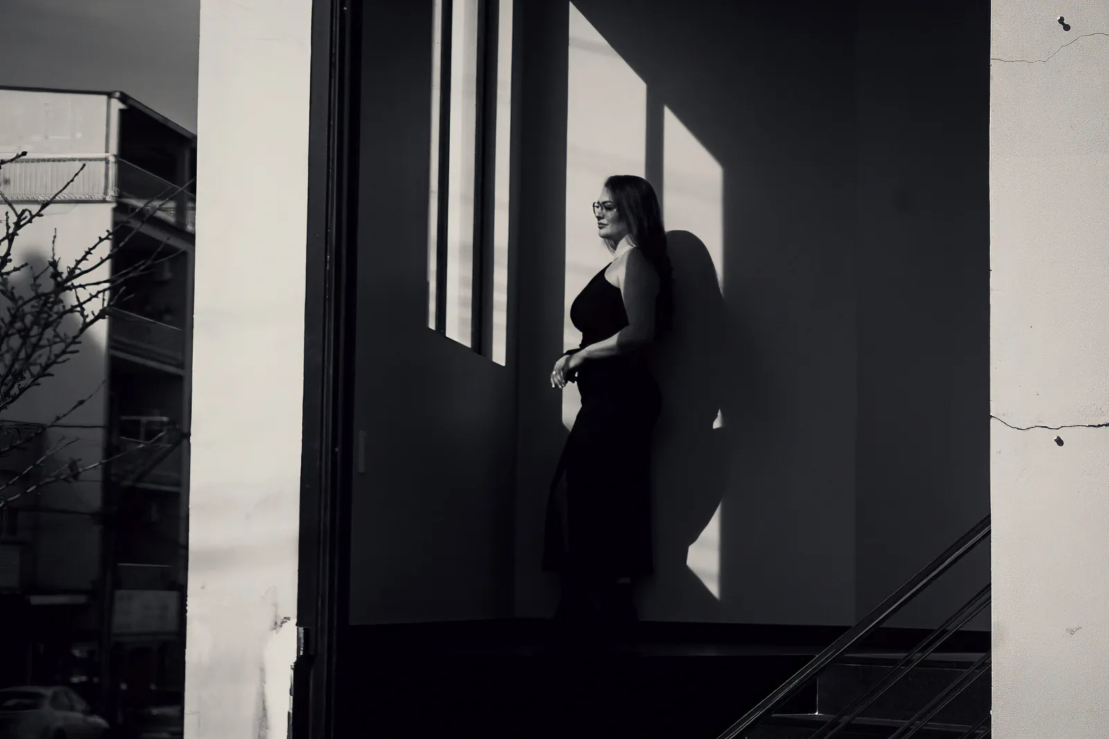 Mulher de vestido preto em janela com luz dura, em preto e branco