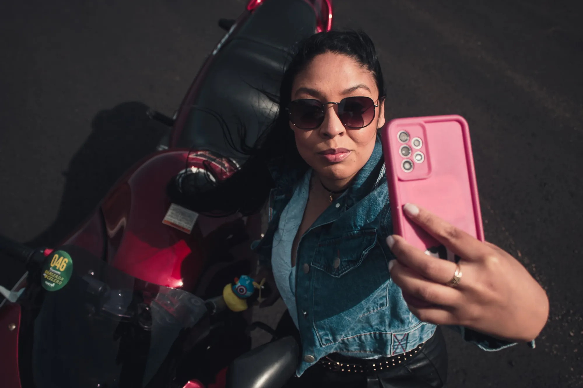 Mulher de óculos escuros faz selfie em moto vermelha
