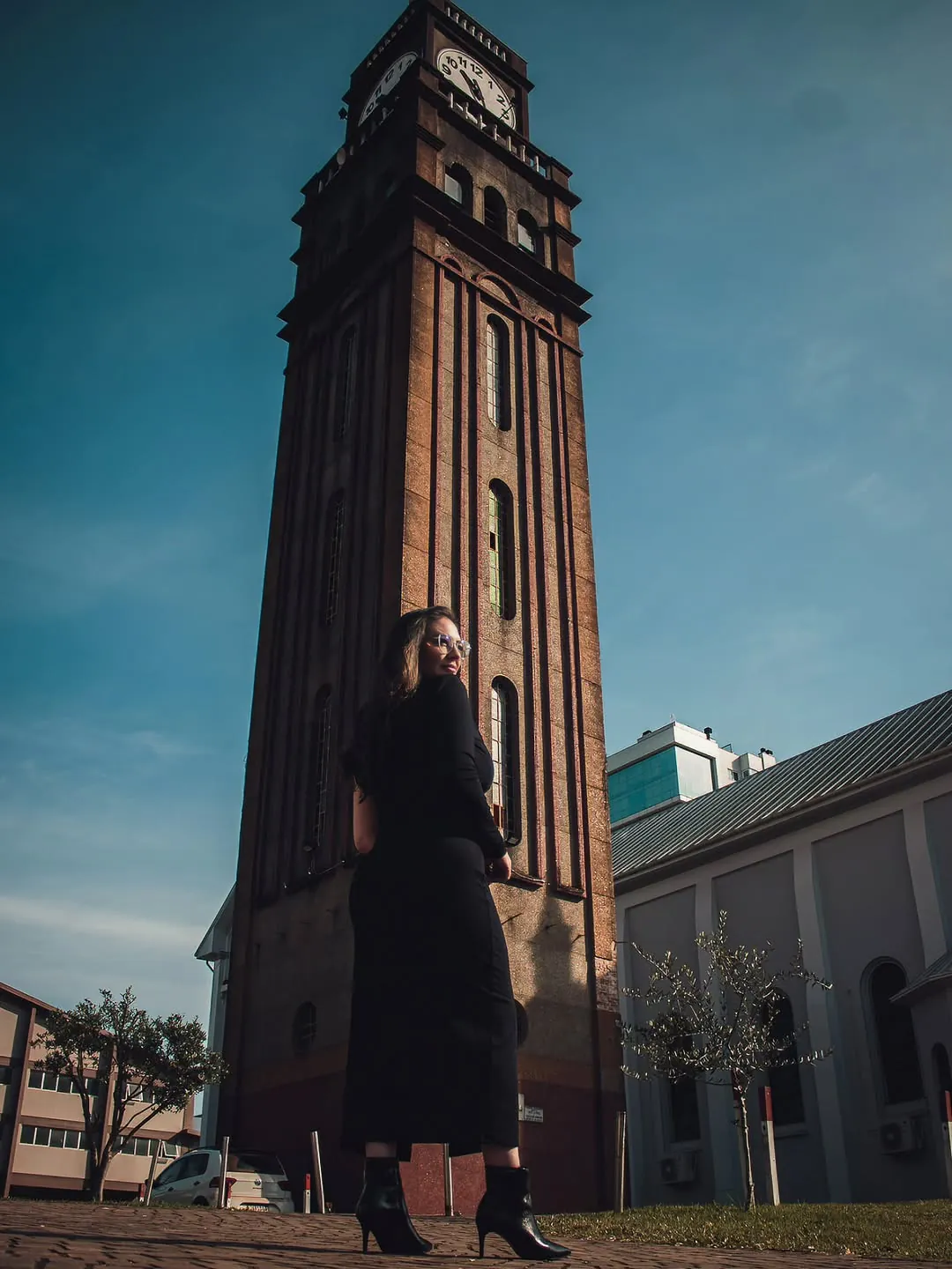 Mulher de vestido preto diante da torre do relógio de Marau