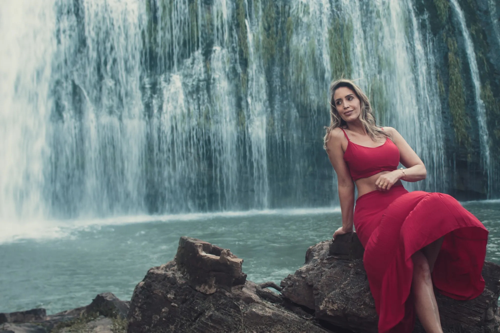 Mulher de vestido vermelho sentada diante de uma cachoeira