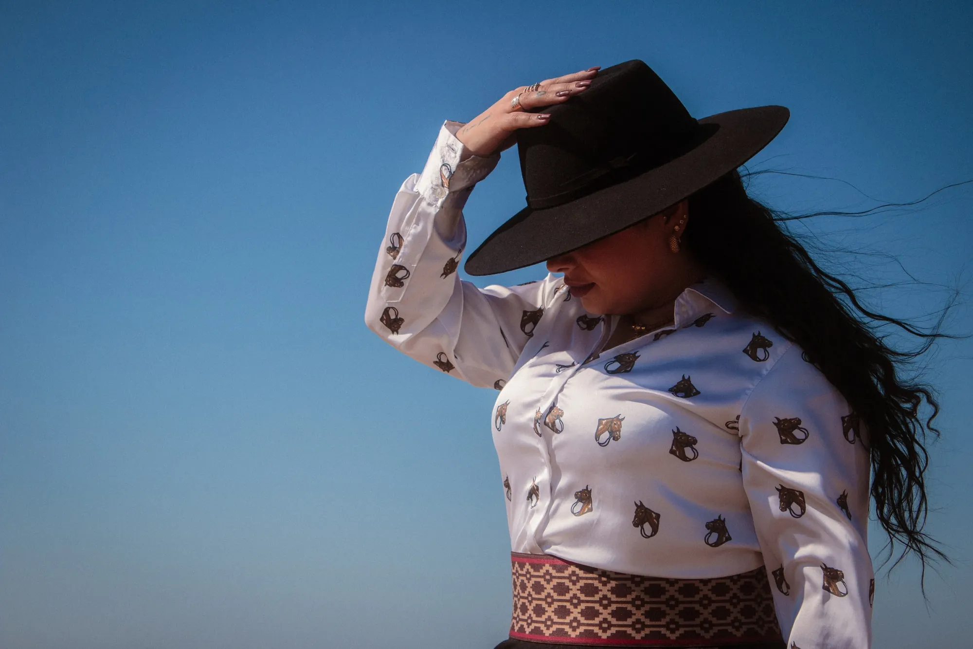Mulher de chapéu preto e camisa branca, mão na aba