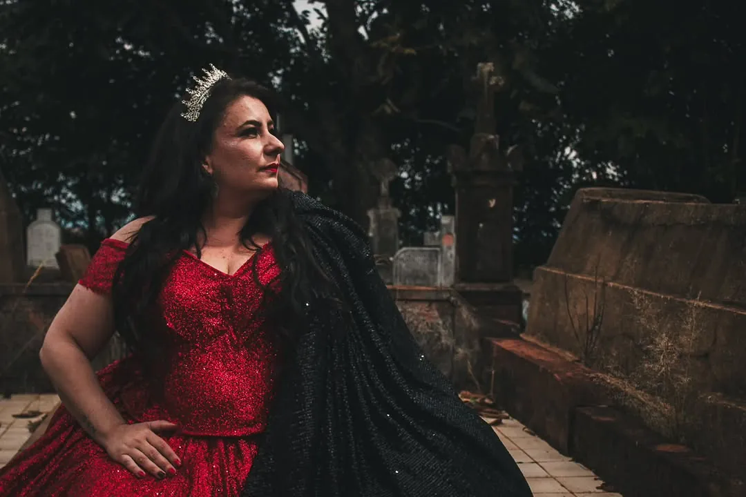 Mulher de vestido vermelho e coroa em cenário antigo