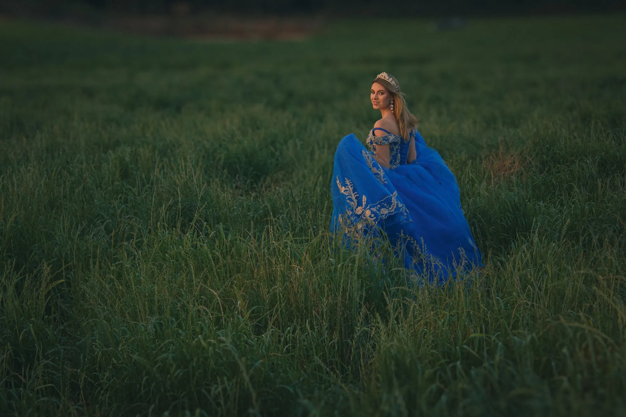 Mulher de vestido azul sentada em campo verde