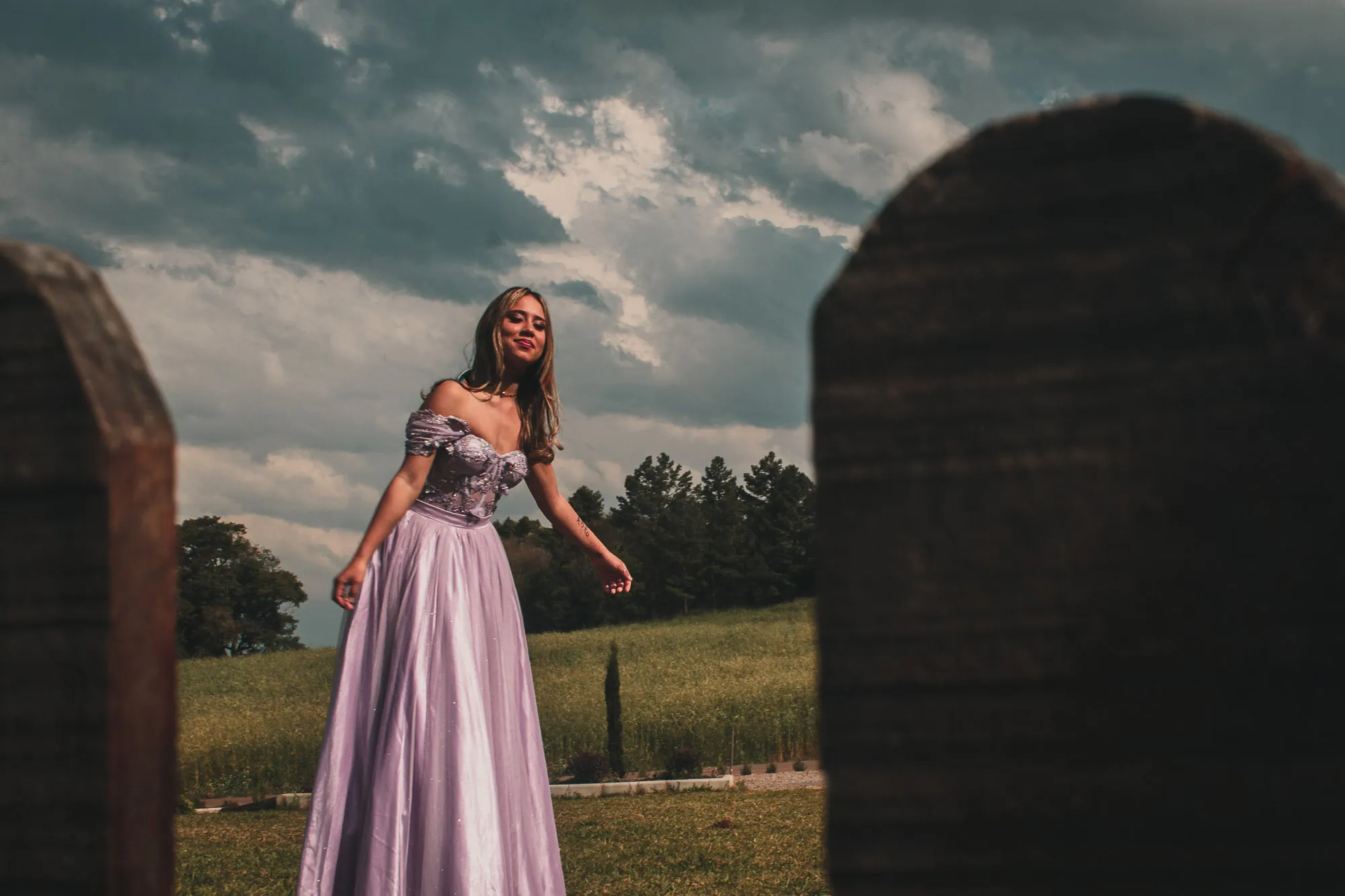 Mulher de vestido lilás em campo, entre lápides antigas